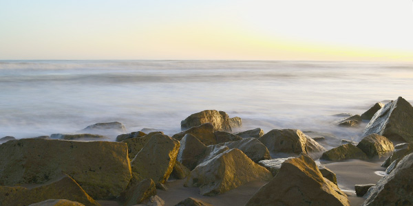 Fotografia de una escena costera con rocas en primer plano y un cielo de atardecer de fondo